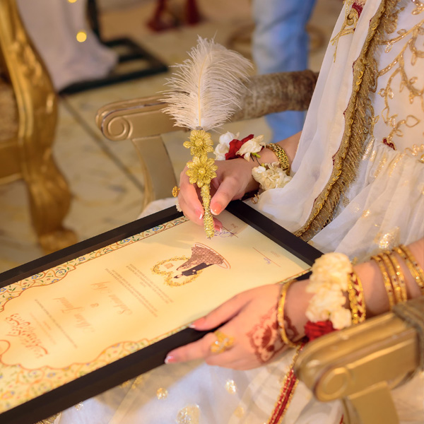 Close-up of a bride's hennaed hand holding a white feather pen while signing the Nikah