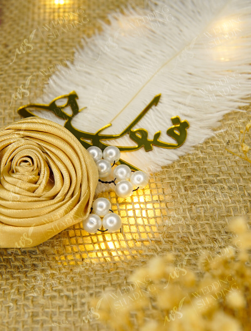 Close view of golden Qubool Hai calligraphy and the folded satin rose