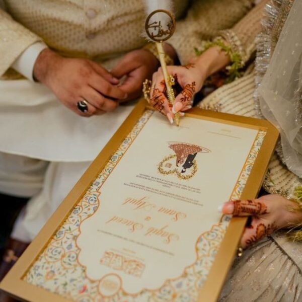 bride's hennaed hand holding a white feather pen while signing the Nikah register