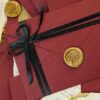 Maroon envelope wedding invitation with black satin ribbon and gold wax seal