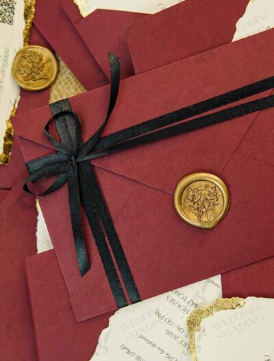 Maroon envelope wedding invitation with black satin ribbon and gold wax seal