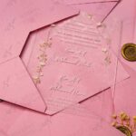 Clear acrylic wedding invitation card with floral arch design on pink envelope