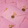 Gold wax seal on soft pink envelope holding the acrylic card